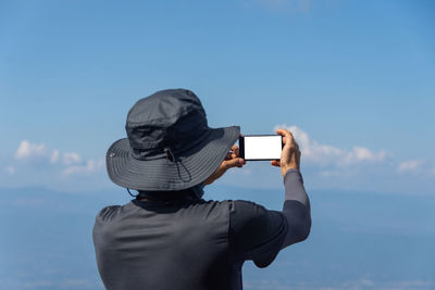 Rear view of man photographing with mobile phone against sky