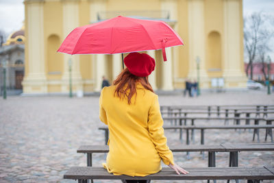 Rear view of woman with umbrella on bench in rainy season