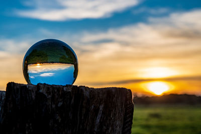 Close-up of crystal ball on shore against sunset sky