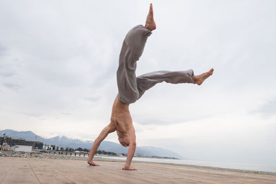 Low section of woman jumping on beach against sky