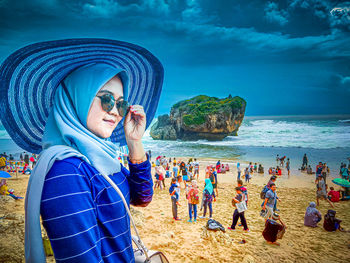 Portrait of young woman using smart phone at beach against sky