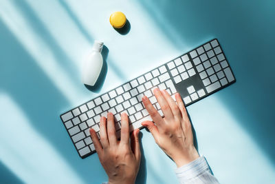 Working zone in sunlight. woman prints on the keyboard, next to the hand cream or sanitizer and cake