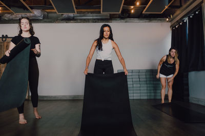 Low angle of calm female athletes in sportswear laying sports mats on wooden floor while preparing to train in spacious gym