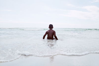 Rear view of shirtless man standing in sea against sky