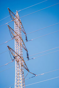 Low angle view of electricity pylon against clear blue sky