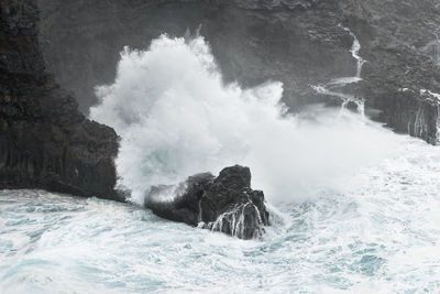 A wave breaks in stormy weather on a rocky coast with a small bay, canary islands, la palma