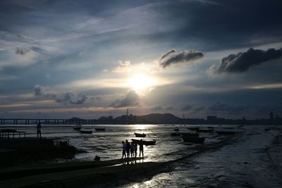 People on shore against sky during sunset