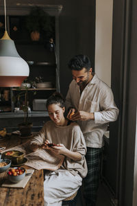 Non-binary person using smart phone by boyfriend at home