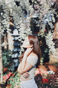 Young woman with eyes closed standing against plants in park