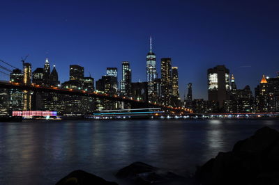 Illuminated buildings by river against sky at night new york