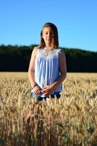 Portrait of teenage girl standing at farm against clear blue sky