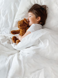 Toddler in bed with teddy bear. little boy under white blanket with fluffy toy. bedtime at home.