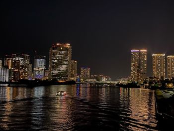 Illuminated buildings by river against sky at night