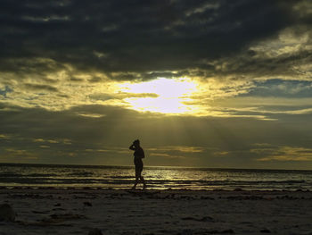 Silhouette man standing on beach against sky during sunset