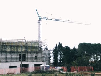 Low angle view of crane by building against clear sky