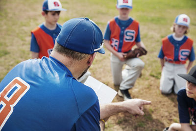 Rear view of coach pointing while discussing with baseball team on field
