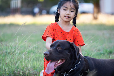 A lovely southeast asian child girl in red outfits plays with her big dog in the back or front yard