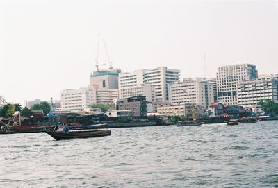 Boats sailing on sea by buildings against clear sky