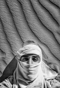 High angle portrait of young man wearing headscarf lying on sand dune