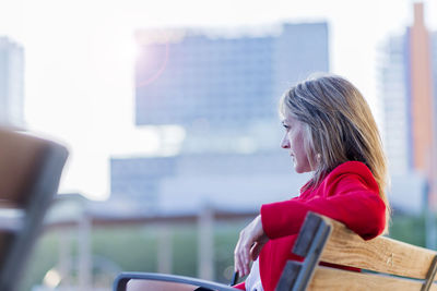 Woman looking away while sitting on bench in city