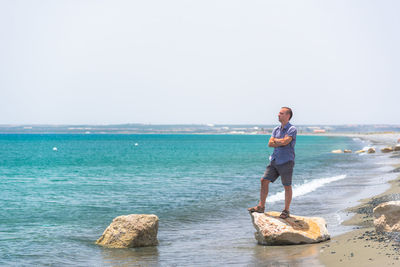 Man standing on rock at beach against clear sky