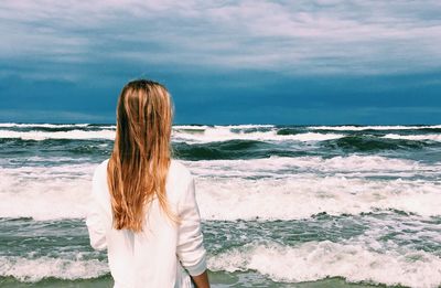 Rear view of woman standing at beach against sky