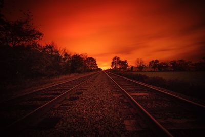 Railroad tracks amidst silhouette trees against sky during sunset