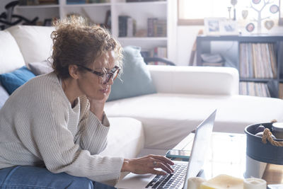 Side view of young woman using mobile phone while sitting at home