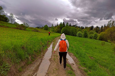 Rear view of man walking on field against sky