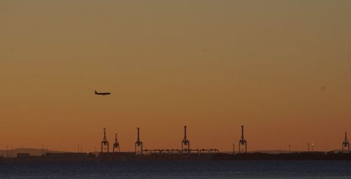 Silhouette airplane flying over sea against sky during sunset