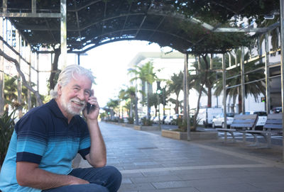 Smiling man talking on phone while sitting outdoors