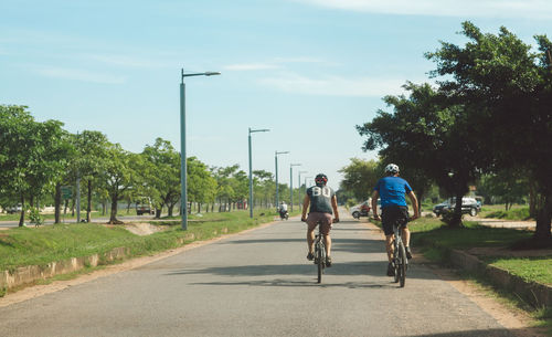 Rear view of people riding bicycle on road