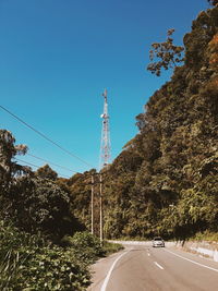 Road by trees against clear blue sky