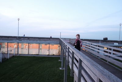 Portrait of woman standing on railing against sky