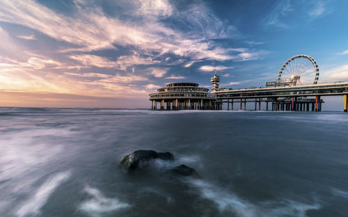 Pier by sea against cloudy sky during sunset