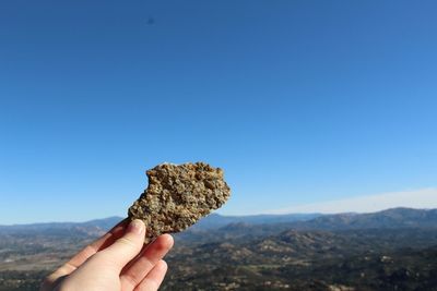 Cropped hand holding rock against clear blue sky