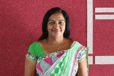 Portrait of mature woman in sari smiling while standing by red wall