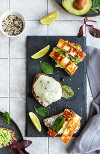 Sandwiches with tartine bread, poached egg, avocado and grilled cheese with salad leaves and lime