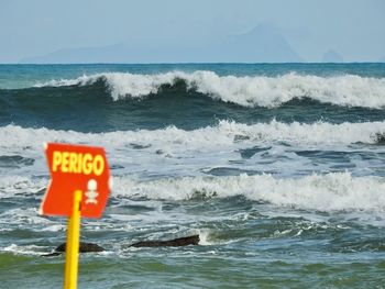 Warning sign by sea against sky