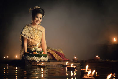 Smiling young woman with religious offerings at lake during night