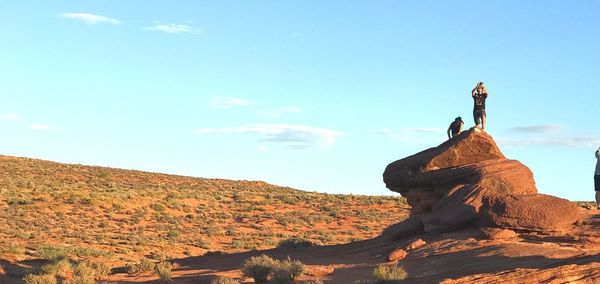 People on rock at desert against sky