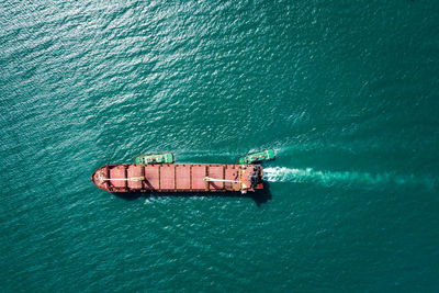 Aerial top view tugboat drag oil ship tanker on green sea going to shipyard repair and maintenance