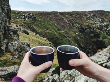 Cropped hands of people holding drinks against mountain range