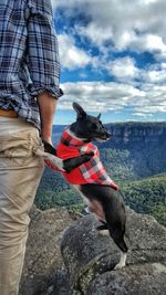 Low section of man holding dog against sky