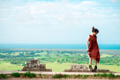 Young woman wearing sunglasses standing on observation point against cloudy sky