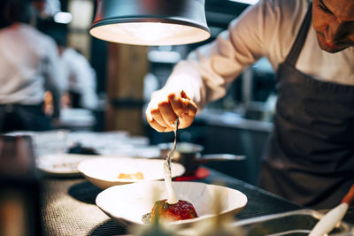 Crop professional chef pouring white sauce on dish in elegant plate working on restaurant kitchen