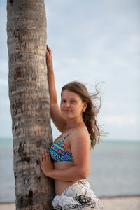 Full length of happy girl on tree trunk by sea against sky