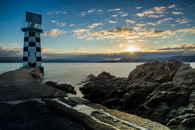 Lighthouse by sea against sky during sunset