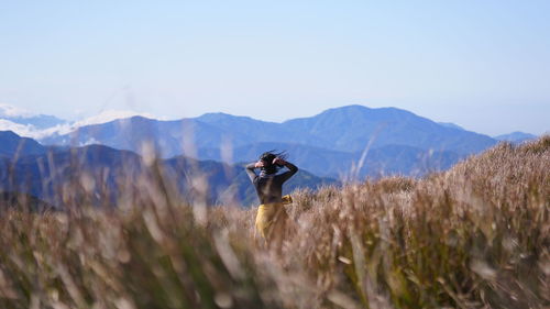 Rear view of young woman amidst grass against sky