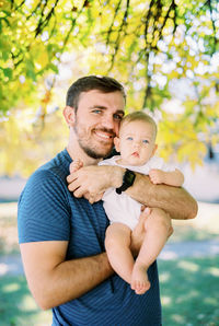 Portrait of young man with arms crossed standing against trees